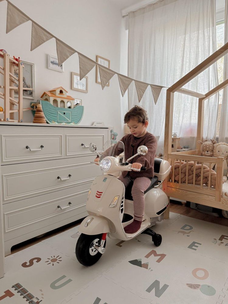 Niño montando la Vespa eléctrica SUN BABY en una habitación infantil.