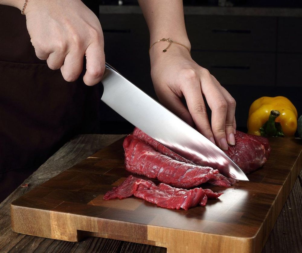 Kochmesser PAUDIN D1 beim Schneiden von rohem Rindfleisch auf einem Holzbrett