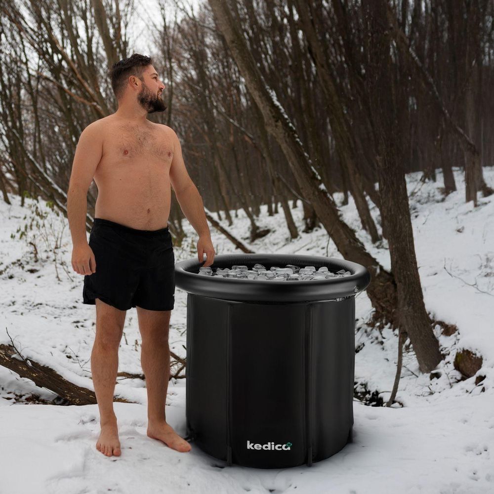 1.jpg: Mann steht barfuß in Badeshorts im Schnee neben der schwarzen kedica Eistonne im Wald