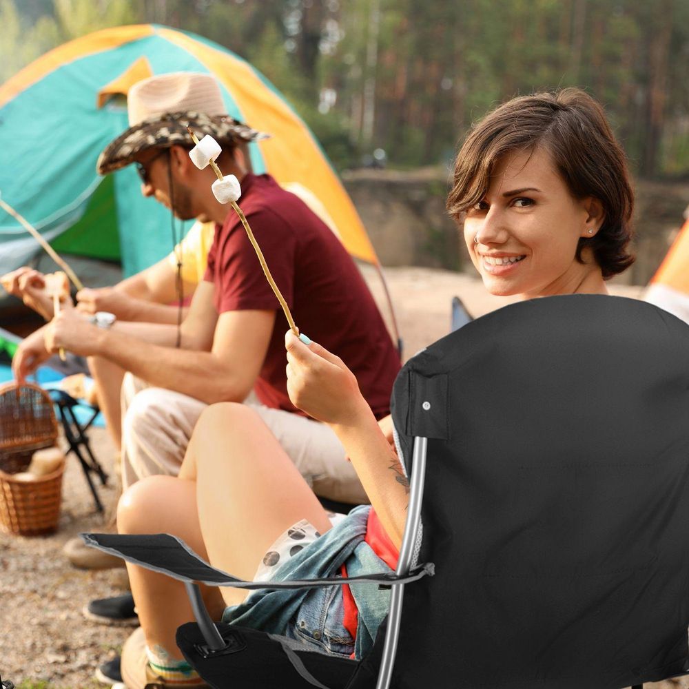 Frau röstet Marshmallows beim Camping, sitzt auf Klappstuhl