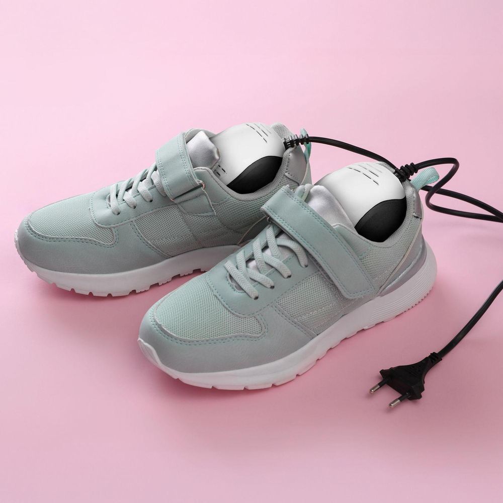Ein Paar hellgraue Turnschuhe mit einem elektrischen Schuhtrockner auf rosa Hintergrund