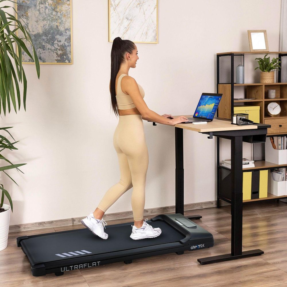 Žena kráča na bežeckom páse a pracuje na notebooku pri vysokom stole