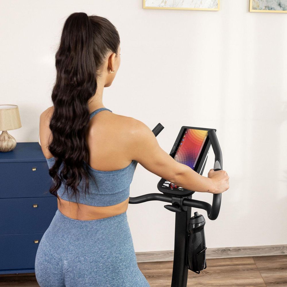 Frau beim Training auf Heimtrainer mit Tablethalter. Unterhaltung beim Sport