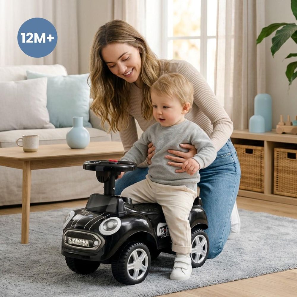 Mutter hilft ihrem Kind beim Sitzen auf dem Rutschauto, Symbol 12M+ sichtbar.