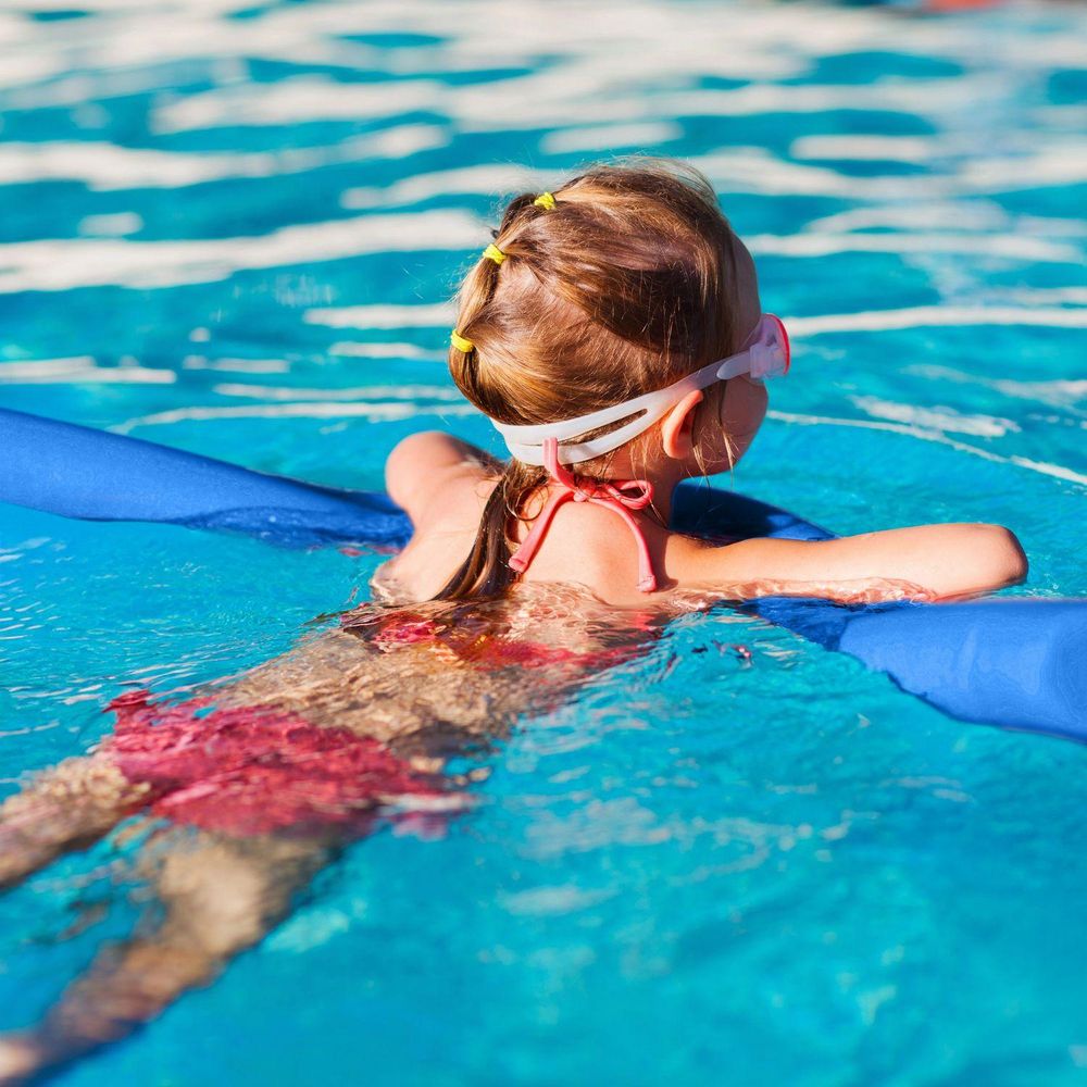 Mädchen von hinten im Pool mit Taucherbrille und blauer Schwimmnudel