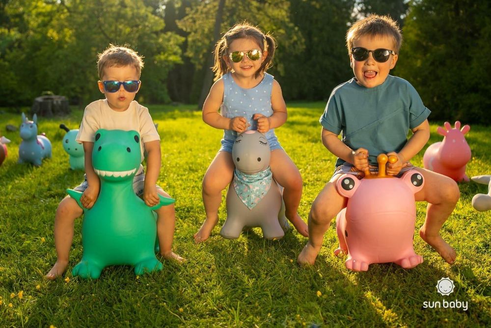 Kinder spielen draußen auf verschiedenen Hüpftieren, darunter das Froschmodell von SUN BABY