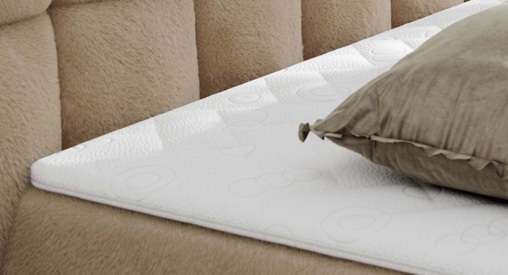 Gestepptes Kopfteil eines beige Bettes. Eine Topper-Matratze liegt auf dem Bett