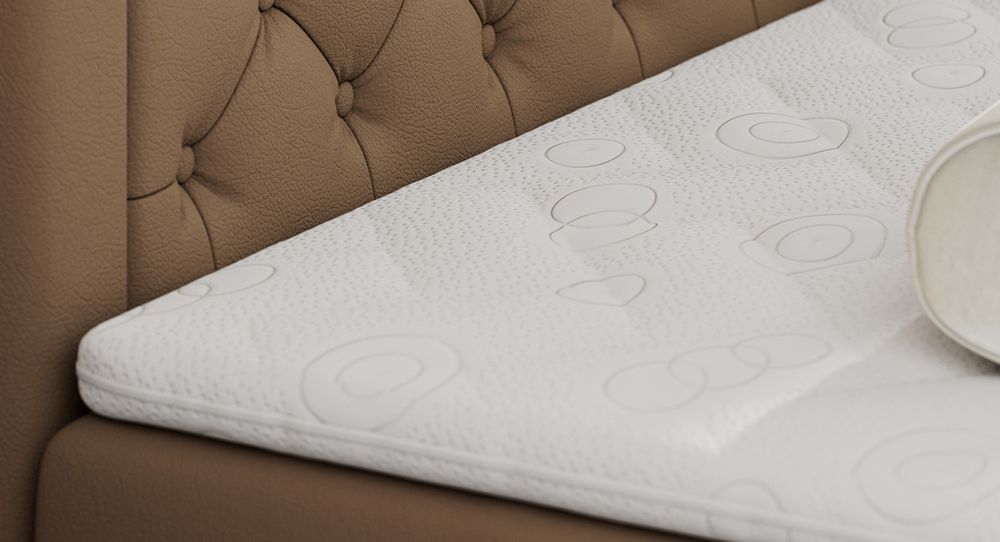 Gestepptes Kopfteil eines beige Bettes. Eine Topper-Matratze liegt auf dem Bett