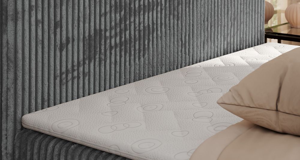 Gestepptes Kopfteil eines grau Bettes. Eine Topper-Matratze liegt auf dem Bett