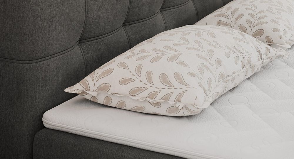 Gestepptes Kopfteil eines grauen Bettes. Eine Topper-Matratze liegt auf dem Bett