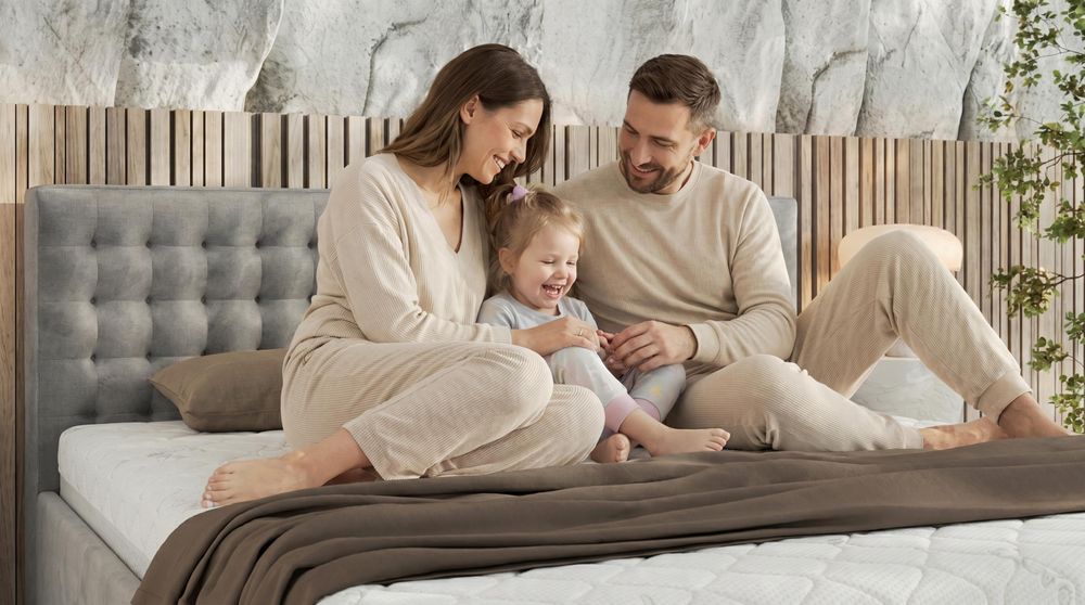 Familie spielt gemeinsam auf beigem Polsterbett im warmen Schlafzimmer.