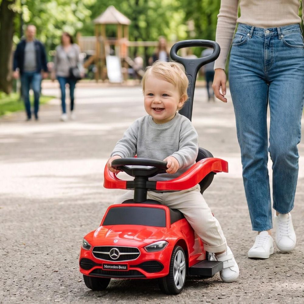 Enfant heureux sur le porteur Mercedes-Benz poussé par un adulte en extérieur