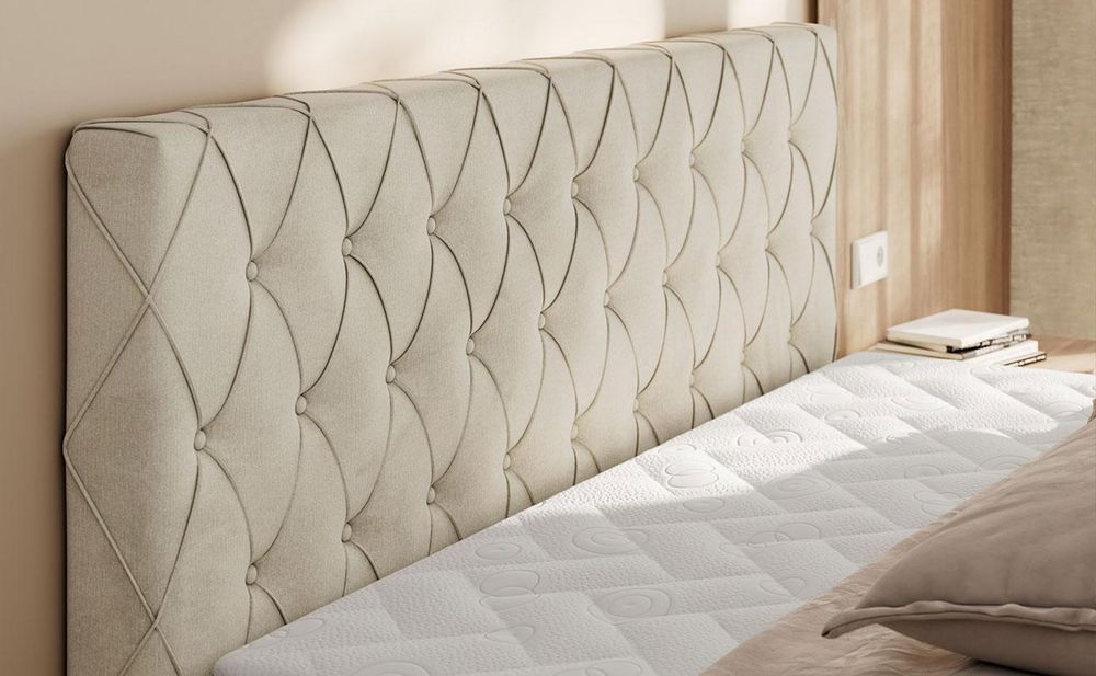 Detailansicht eines grauen Boxspringbetts mit gepolstertem Kopfteil im geometrischen Steppmuster.