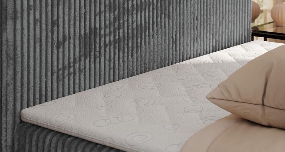 Gestepptes Kopfteil eines grau Bettes. Eine Topper-Matratze liegt auf dem Bett