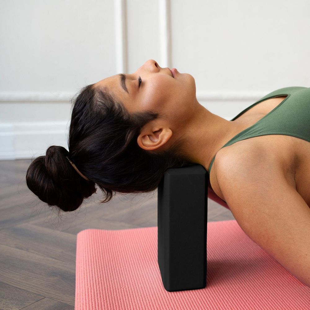 Frau entspannt auf Yogamatte, Kopf auf Yogablock gestützt