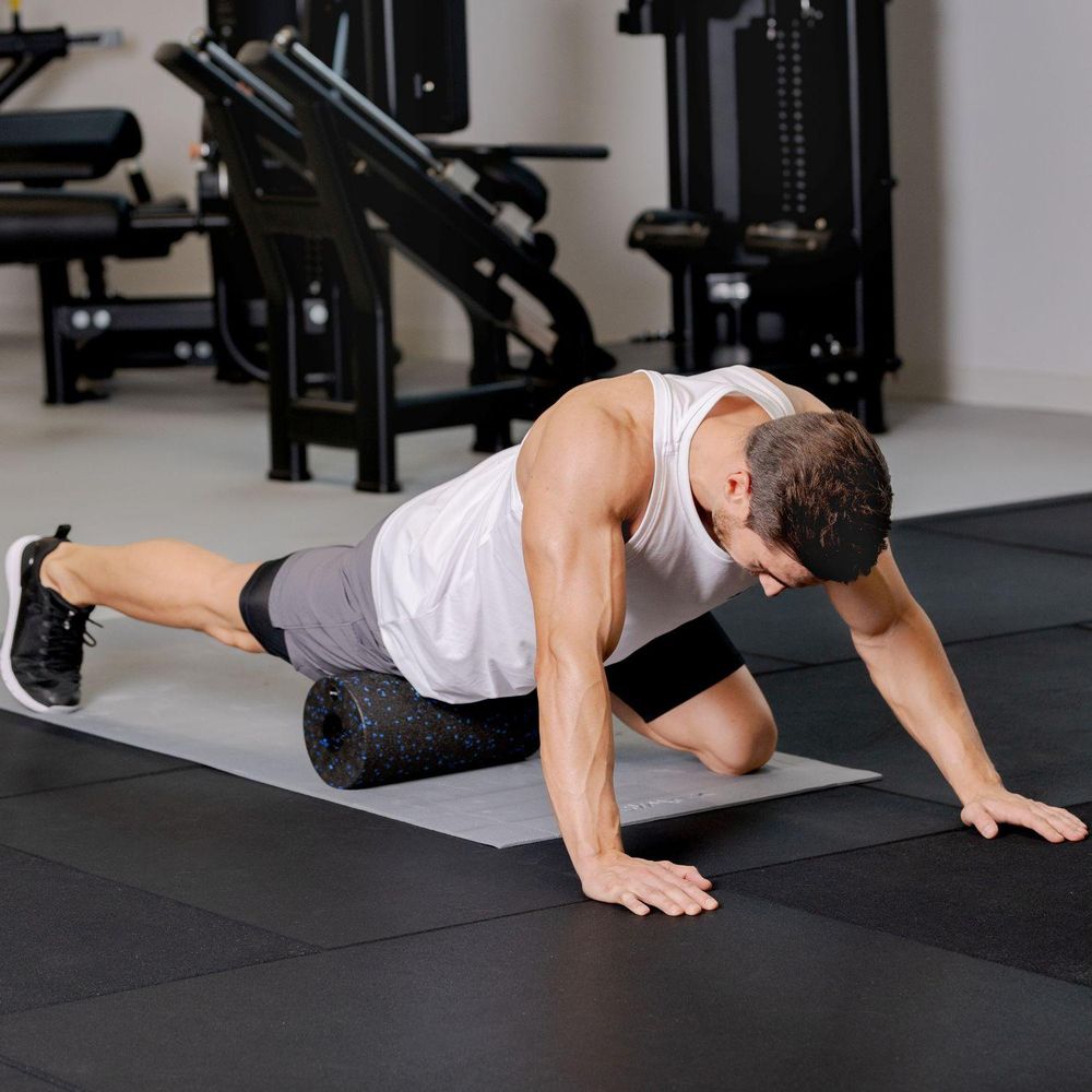 Mann massiert Bein mit Faszienrolle auf der Matte im Fitnessstudio