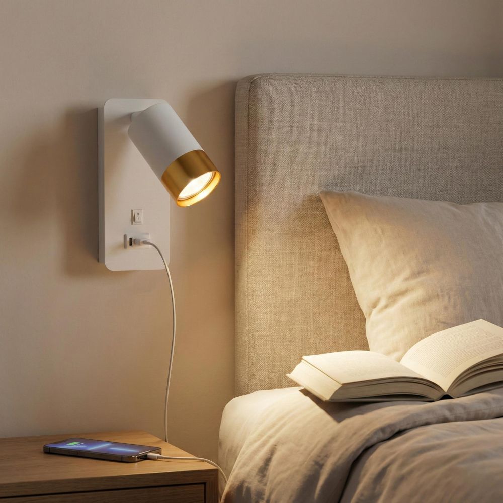 LED-Wandleuchte mit USB-Anschluss und Goldspot, montiert neben einem gepolsterten Bettkopfteil.
