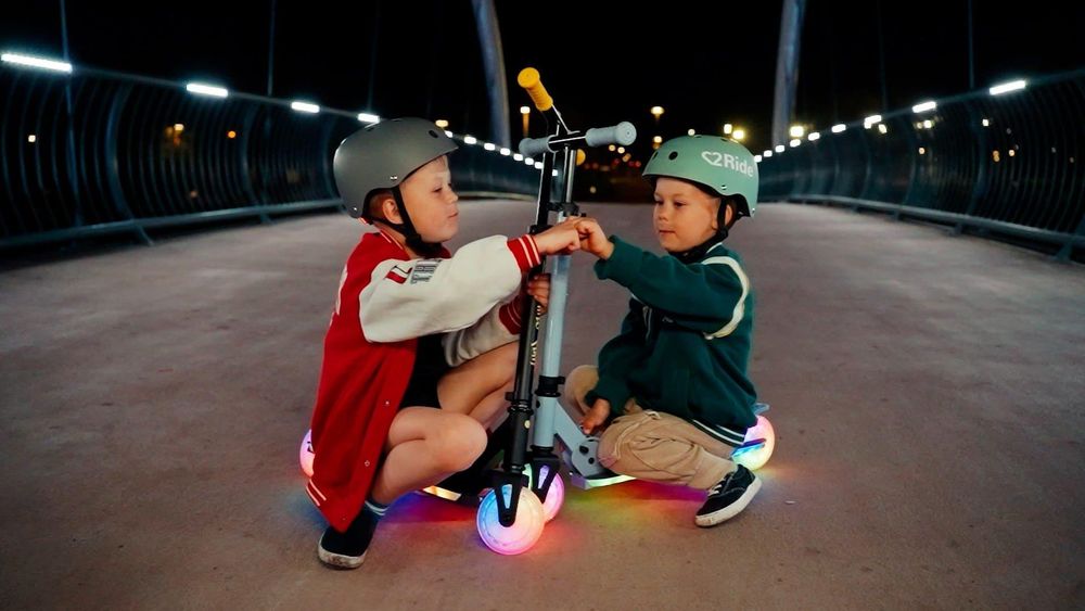 Bambini che giocano con il monopattino Lumiride illuminato di sera.