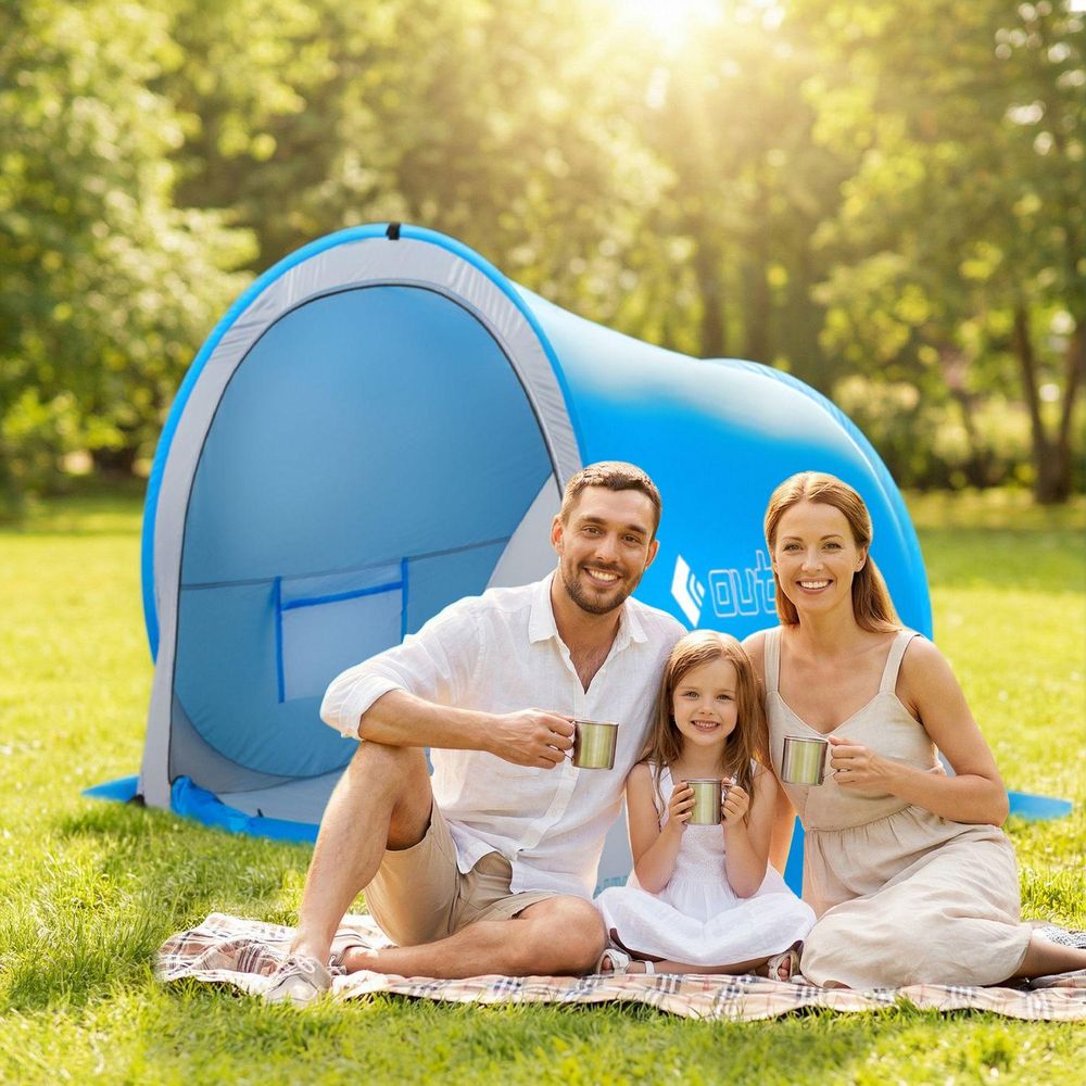 Lächelnde Familie mit Kind vor blauem Pop-up-Zelt auf einer Wiese
