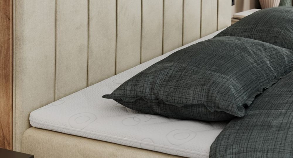 Gestepptes Kopfteil eines beige Bettes. Eine Topper-Matratze liegt auf dem Bett