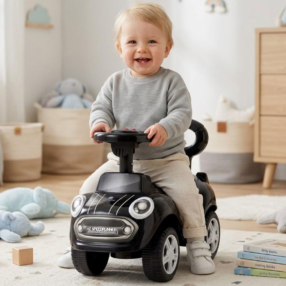 Kleinkind sitzt lachend auf dem schwarzen Rutschauto im Kinderzimmer.