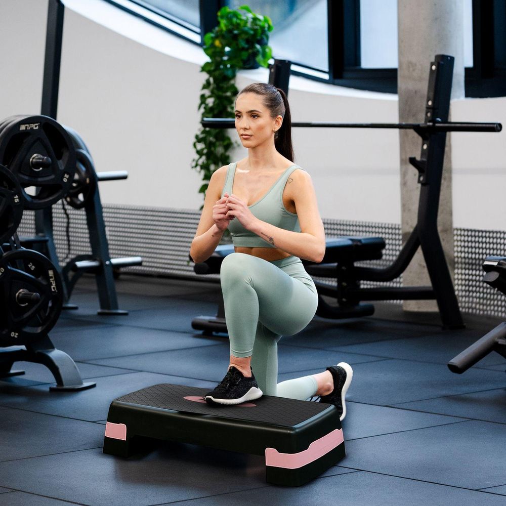 Frau macht Ausfallschritt auf dem Stepper im Fitnessstudio