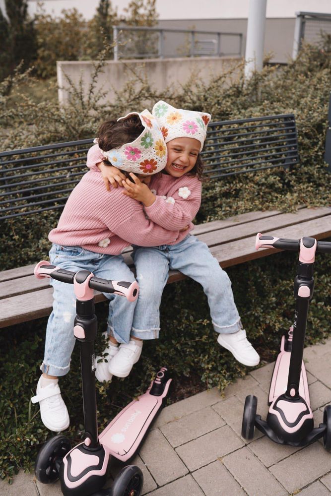 Dos niños sentados juntos con sus patinetes SUN BABY en un parque