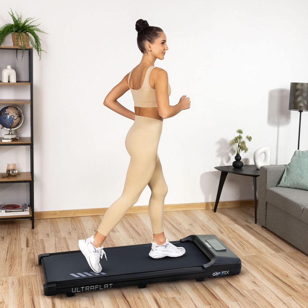 Sportliche Frau joggt auf einem kompakten Laufband im Wohnzimmer.