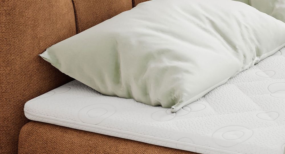 Gestepptes Kopfteil eines orange Bettes. Eine Topper-Matratze liegt auf dem Bett