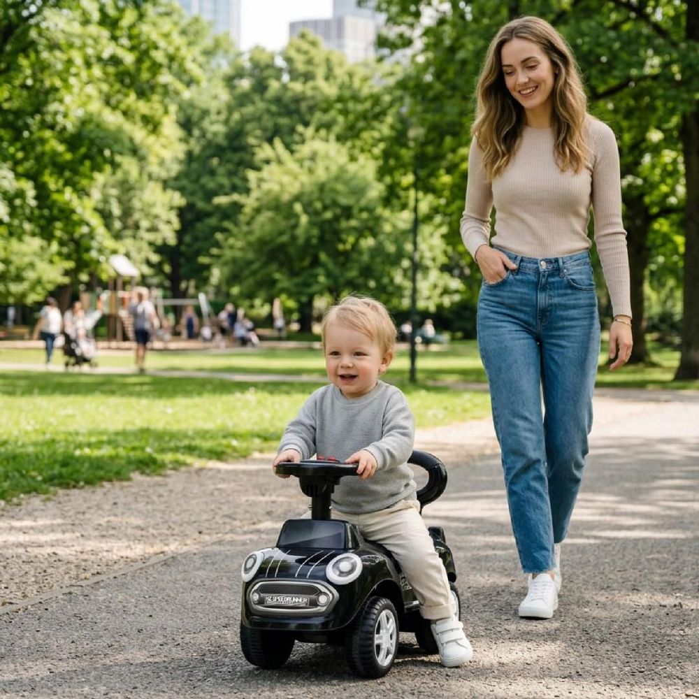 Kind fährt das Rutschauto draußen im Park, Mutter begleitet es auf dem Weg.