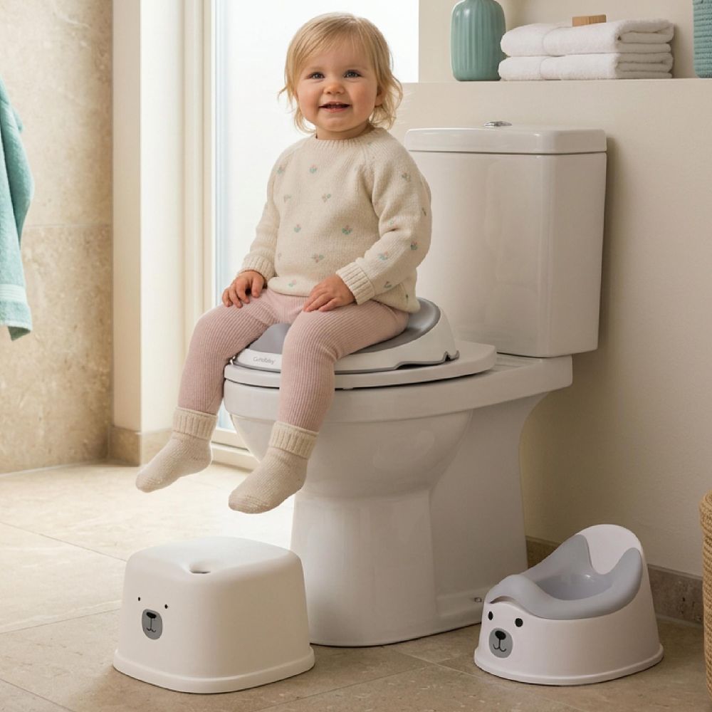 Niña sentada en el adaptador de inodoro con taburete y orinal en el suelo del baño.