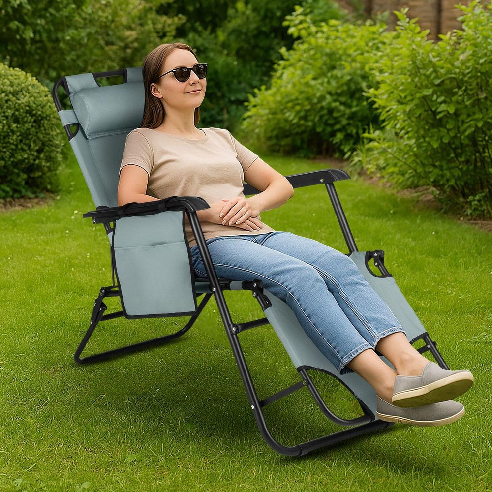 Frau mit Sonnenbrille entspannt auf hellgrauem Gartenliegestuhl im Grünen