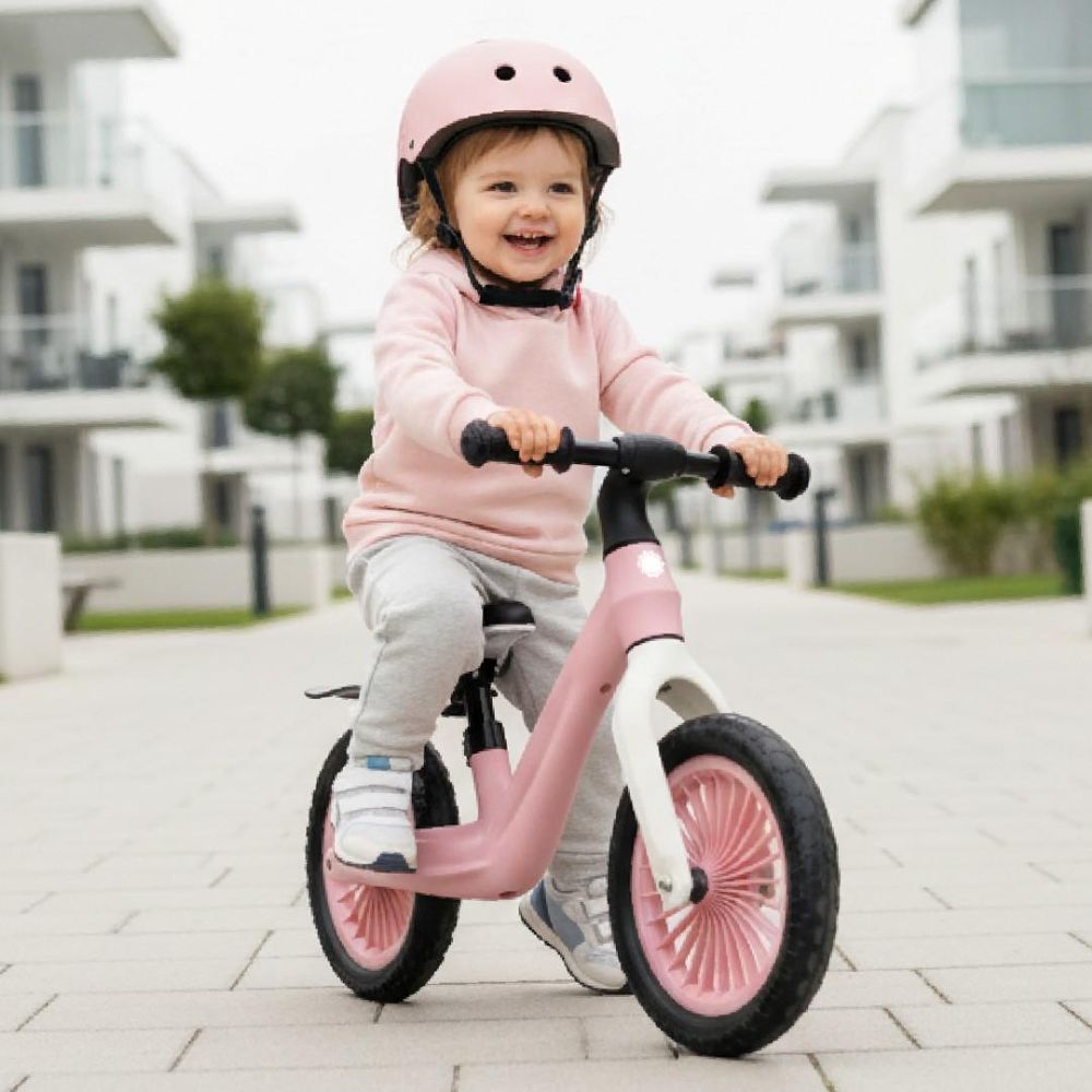 Niña montando la bicicleta sin pedales Sun Baby Sport rosa en la calle.