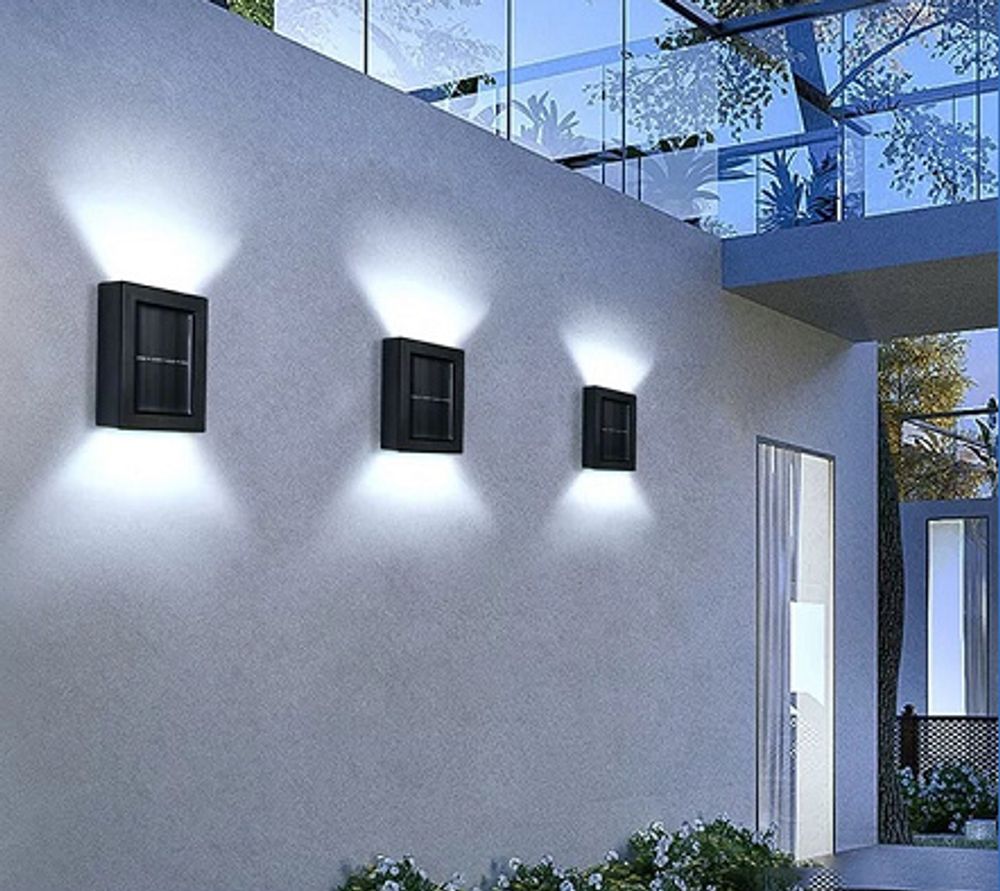 Drei schwarze Solar-Wandleuchten beleuchten eine weiße Außenwand.