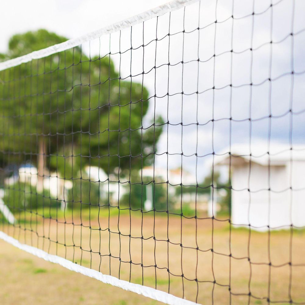 Volleyballnetz auf einem Spielfeld mit Bäumen und Gebäuden im unscharfen Hintergrund