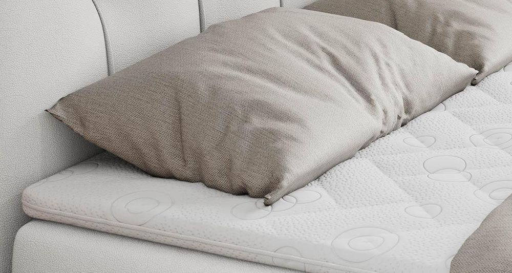 Gestepptes Kopfteil eines grau Bettes. Eine Topper-Matratze liegt auf dem Bett