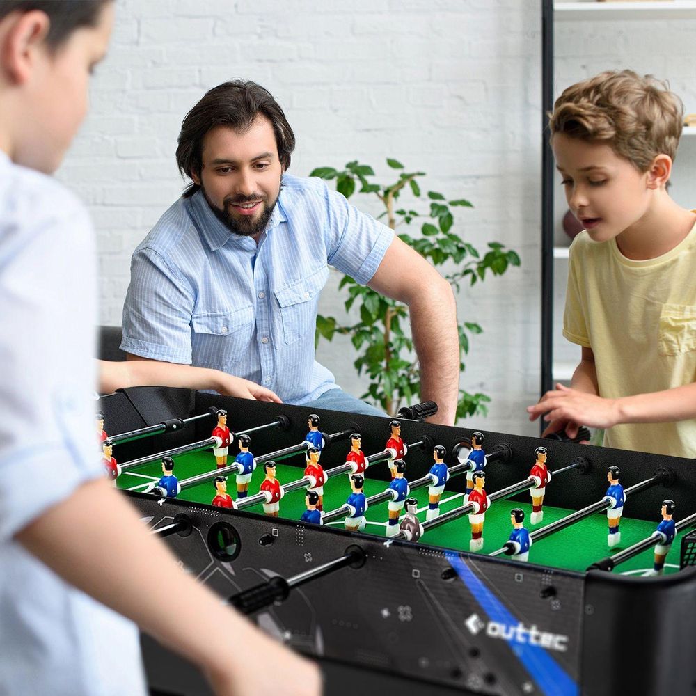 Vater spielt mit zwei Jungen (Kindern) eine Partie Tischfußball, alle lächeln