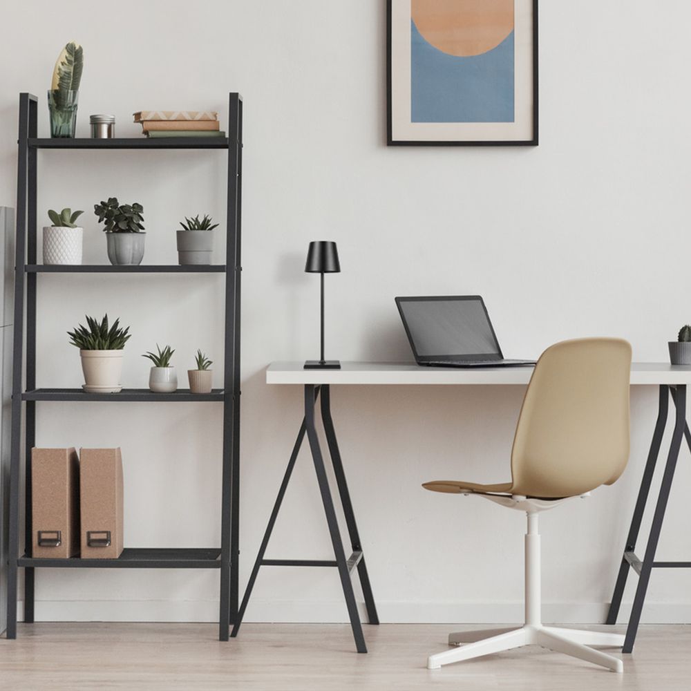 Lampe auf dem Schreibtisch im Zimmer, neben Laptop und Stuhl, minimalistische Einrichtung.