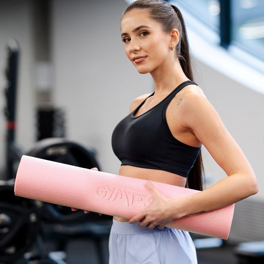 Eine lächelnde Frau, die eine aufgerollte rosa Yogamatte hält