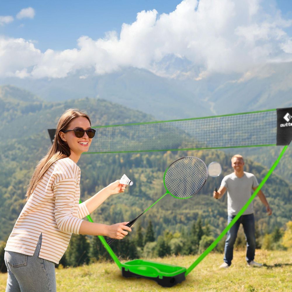 Frau spielt Badminton mit lächelndem Mann im Hintergrund, Berge im Hintergrund