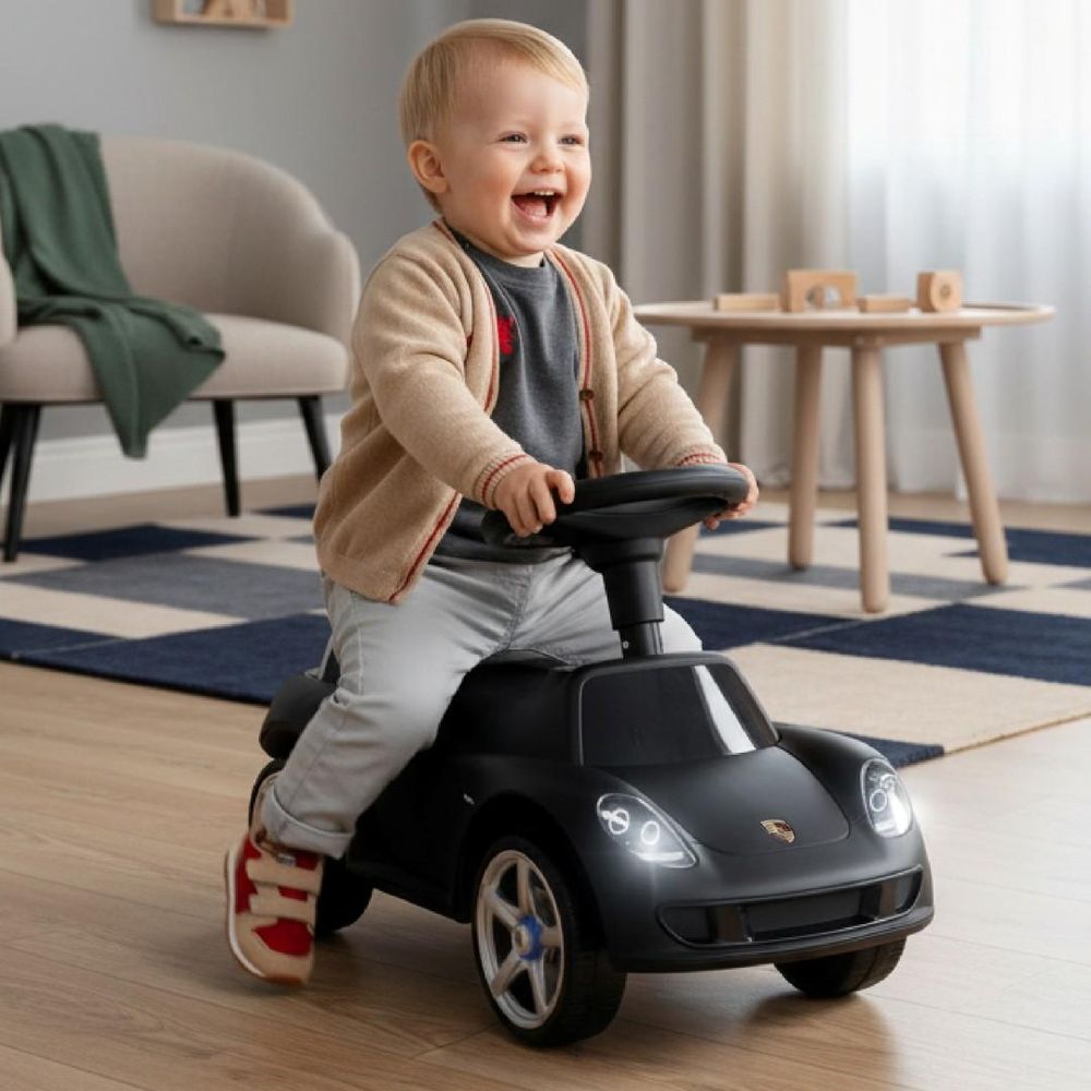 Enfant souriant assis sur le porteur SUN BABY noir, phares allumés.