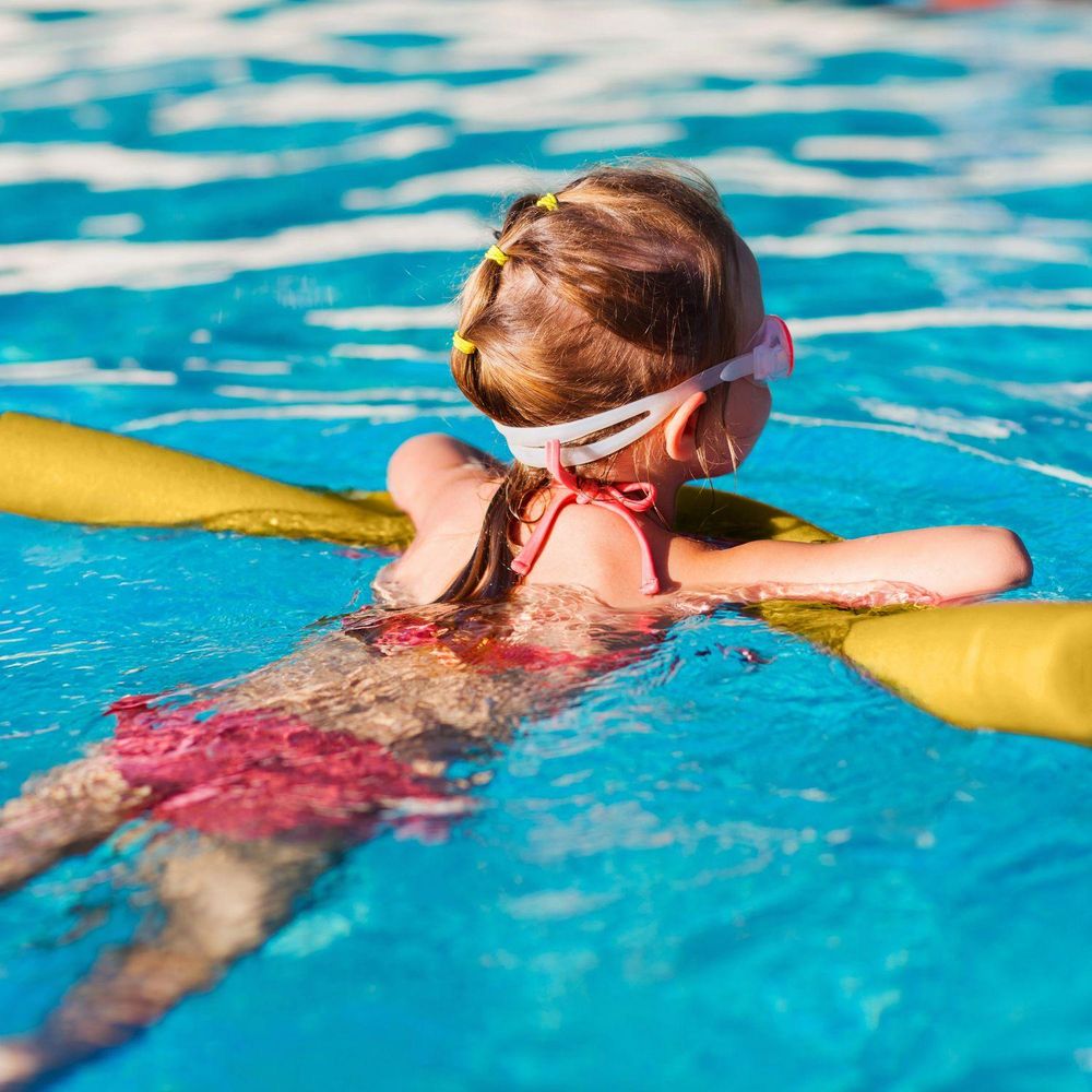 Mädchen von hinten im Pool mit Taucherbrille und gelber Schwimmnudel