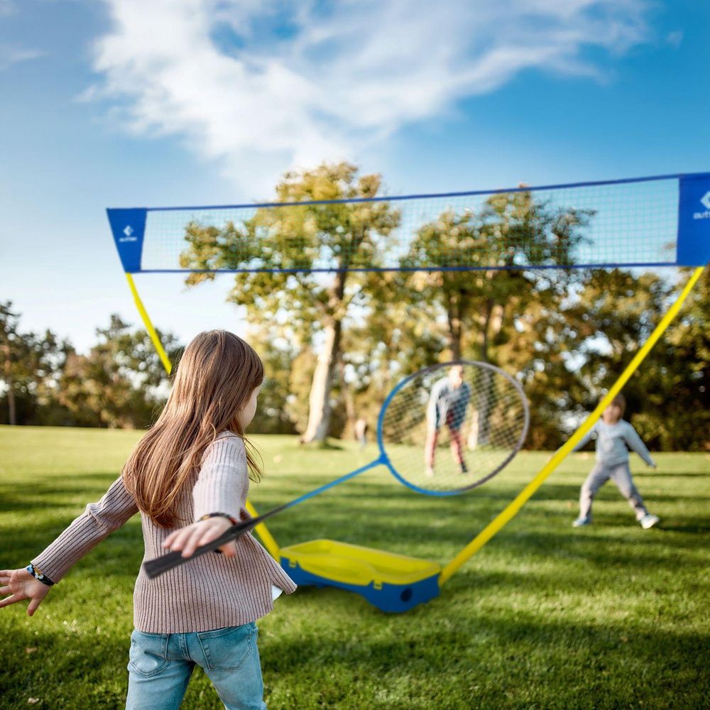 Mädchen spielt Badminton im Park, im Hintergrund Netz und andere Kinder
