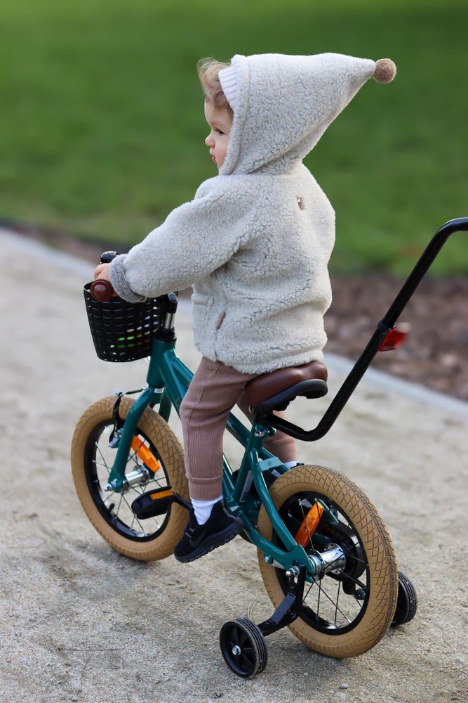 Vista trasera de la bicicleta infantil con niño, mostrando barra de empuje y reflectantes.