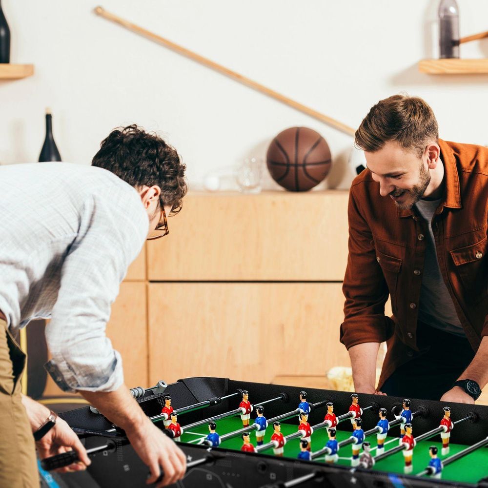 Zwei junge Männer spielen Tischfußball und lächeln sich über den Tisch hinweg an