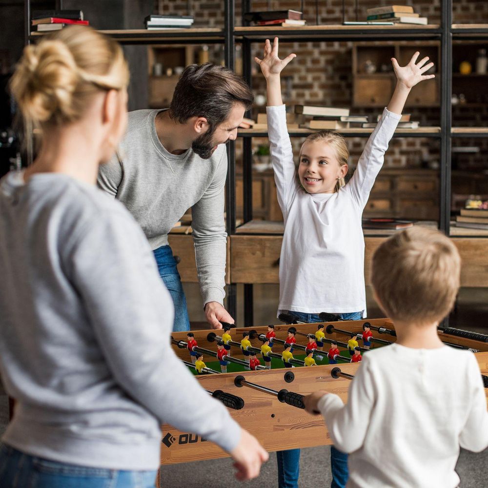 Familie spielt Tischfußball; Mädchen jubelt mit erhobenen Armen