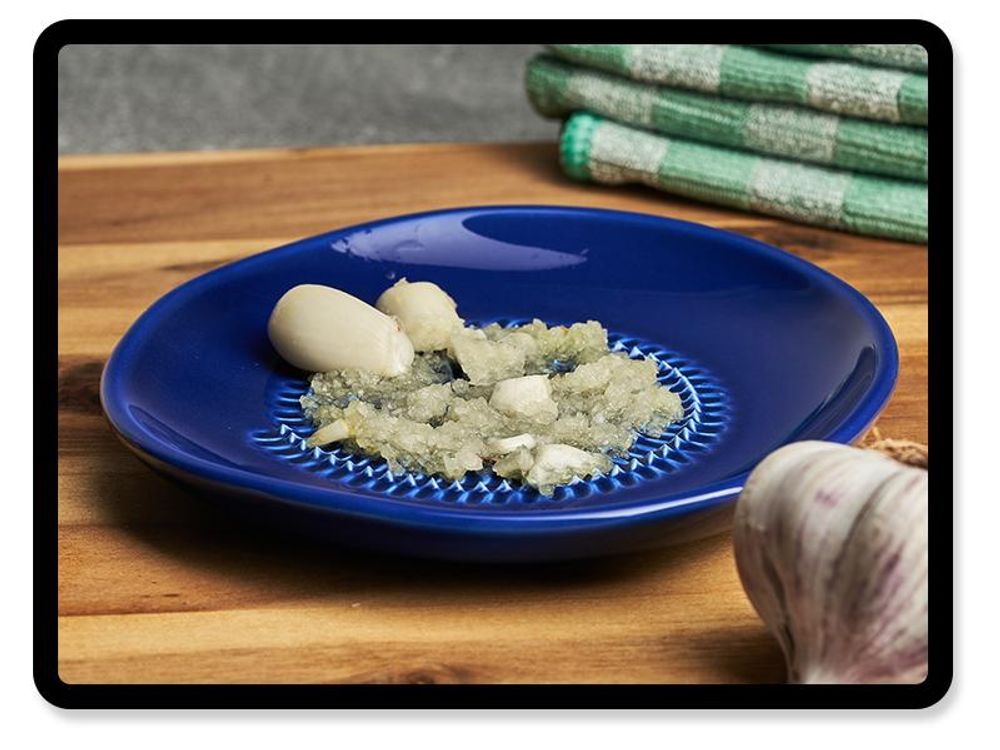 Geriebener Knoblauch in der blauen Keramikreibe von TURBO PRODUKTE auf Holzbrett