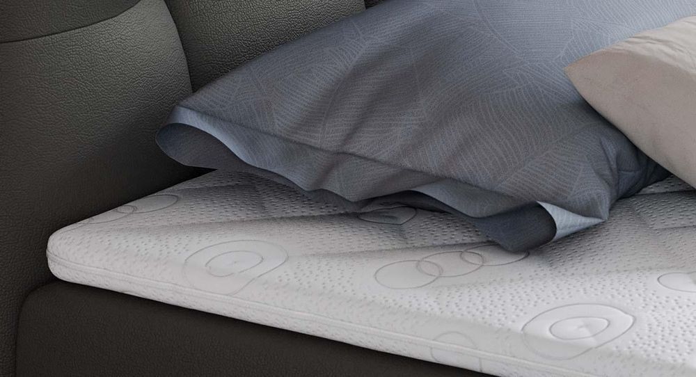 Gestepptes Kopfteil eines grau Bettes. Eine Topper-Matratze liegt auf dem Bett