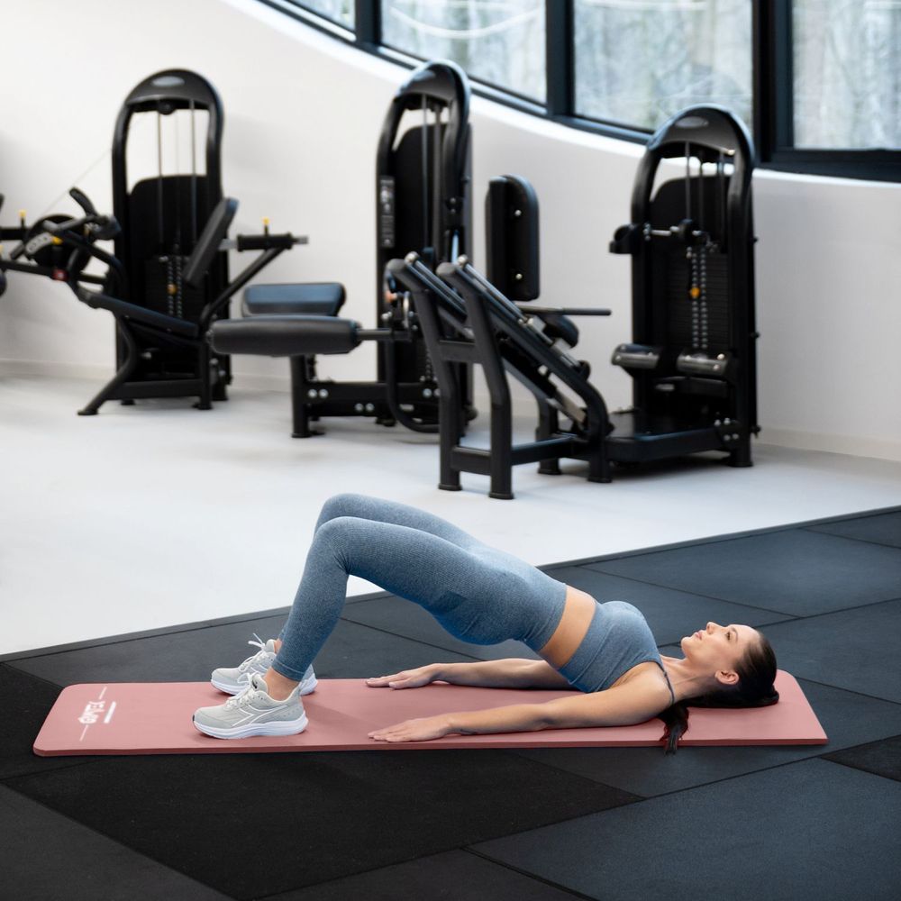 Frau macht Hüftbrücke auf rosa Fitnessmatte im Gym.