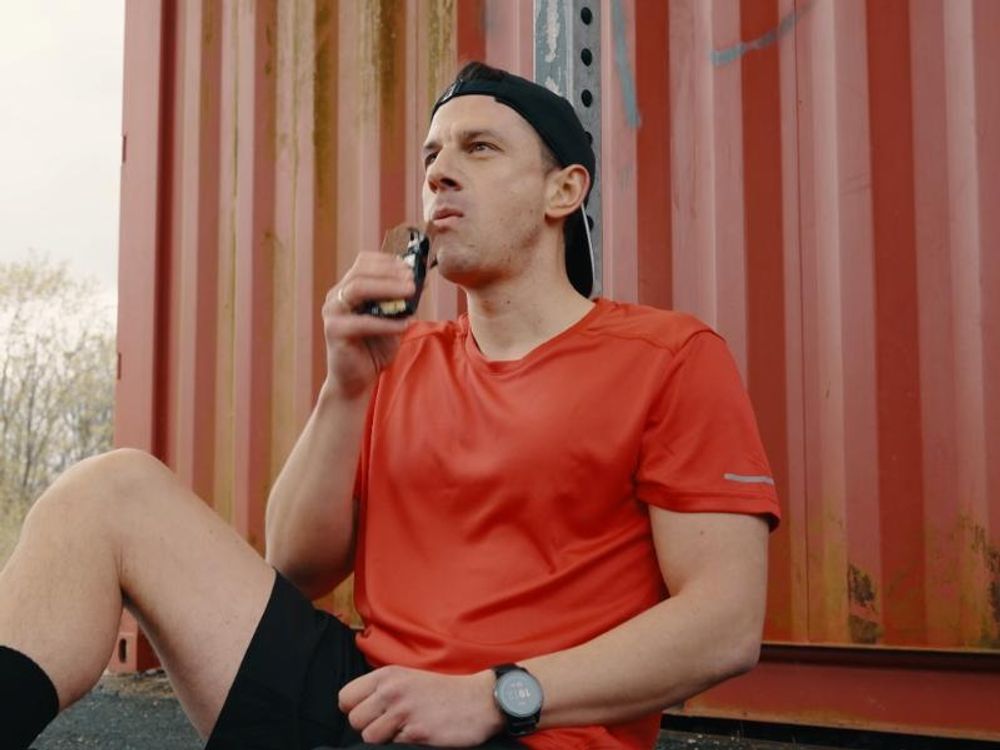 Sportler sitzt vor einem Container und isst einen Big Block Proteinriegel